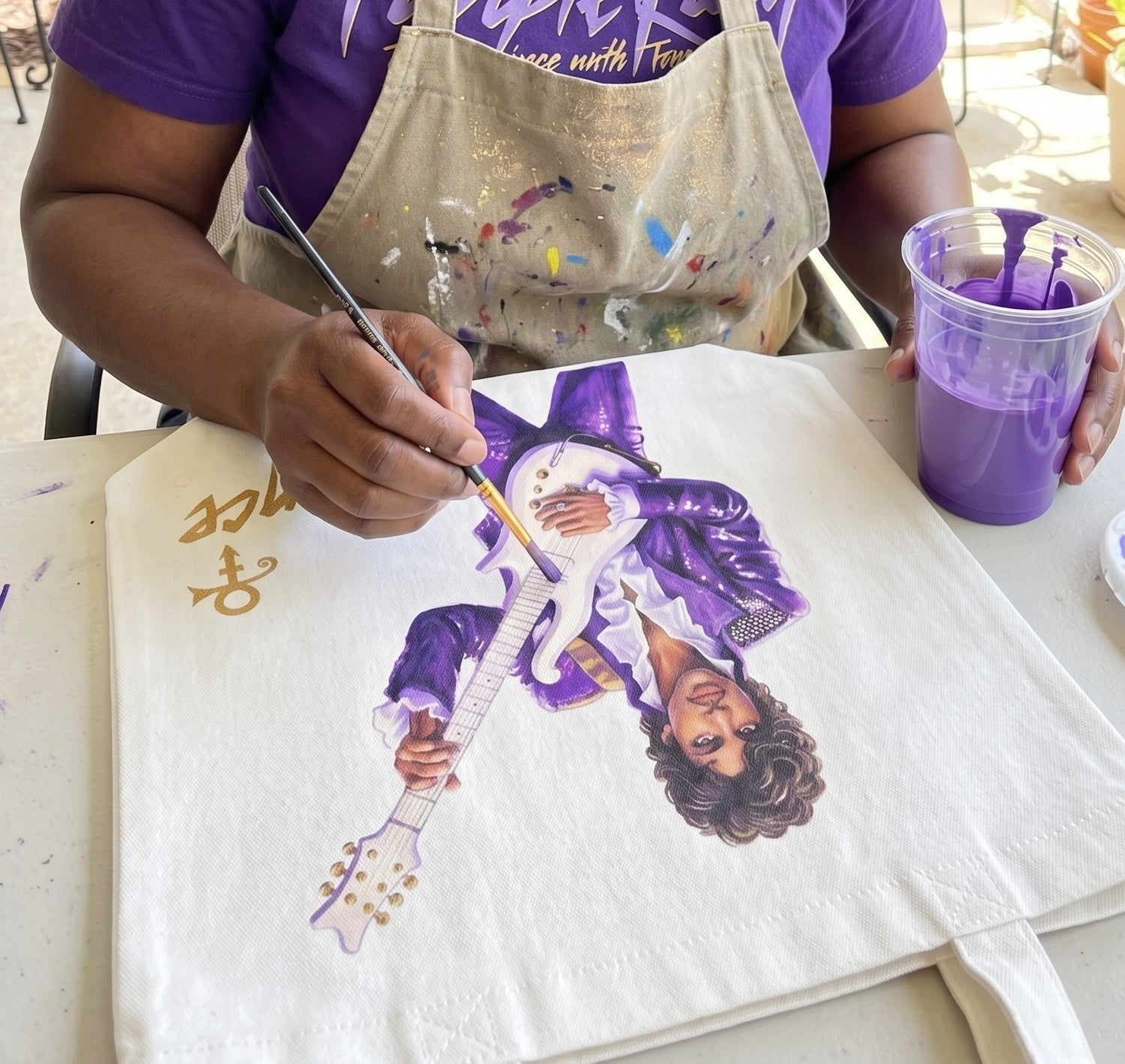 Hands painting a Prince tribute tote bag